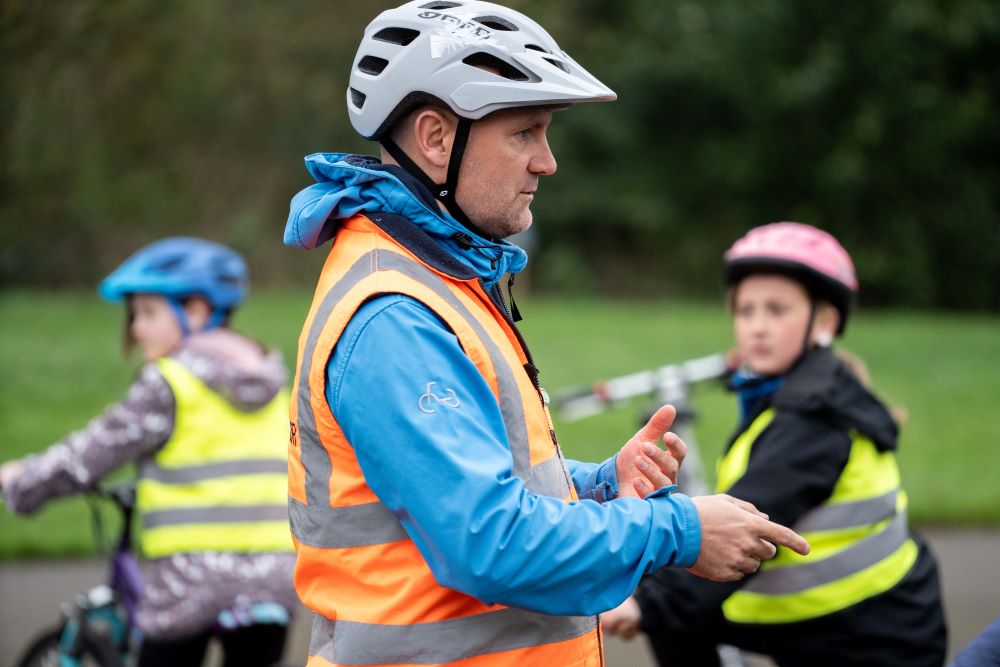 Instructor in playground with riders in the background on their cycles