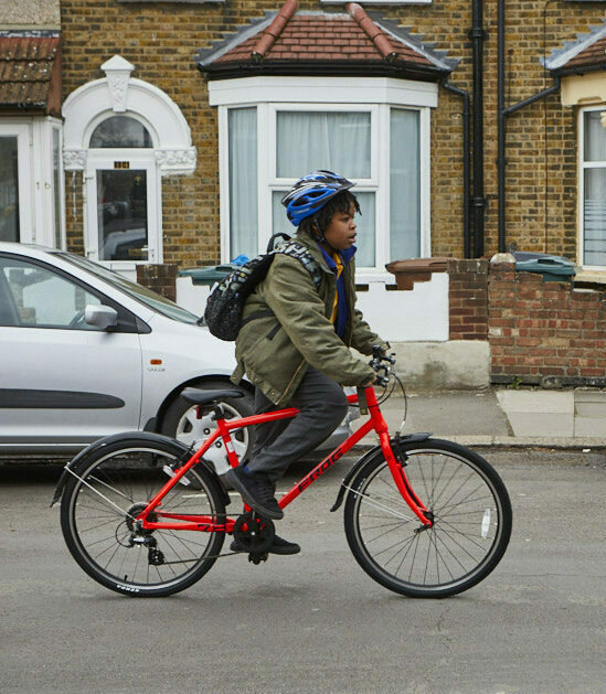 A boy wearing a green jacket and blue helmet cycles along a residential street on a red bike.