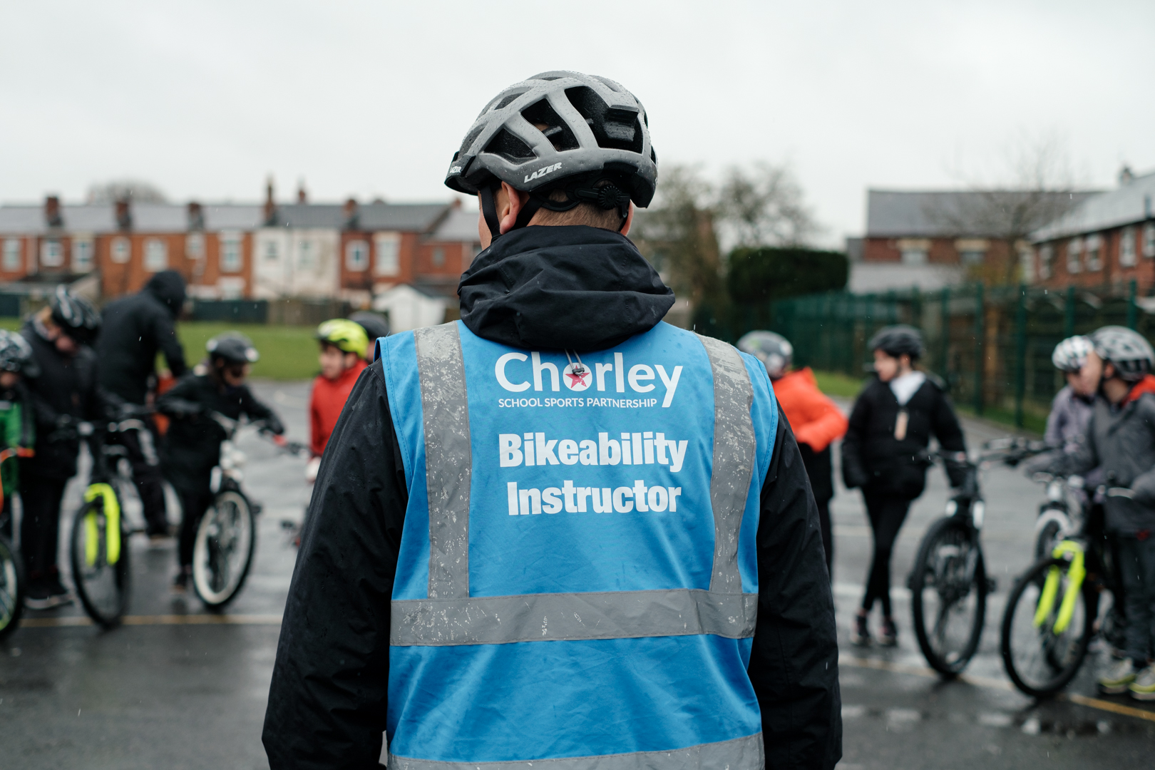 An instructor is standing facing a group of Bikeability riders with their cycles in the playground