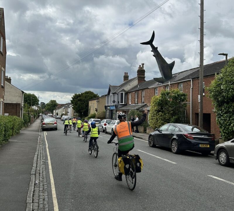 Instructor Kate Arnold is cycling behind a group of Bikeability riders who are cycling on the road for a lesson