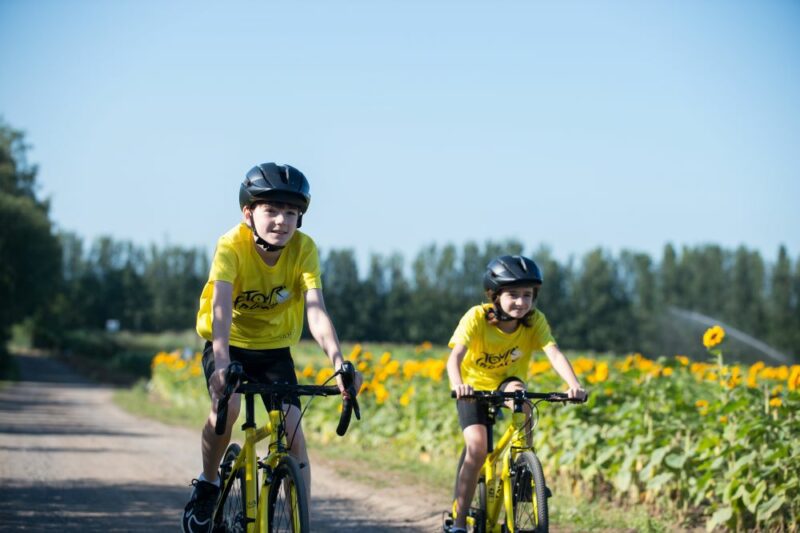 Two children, a boy and a girl, cycling on Frog Tour de France branded bicycles. They are both wearing yellow Tour de France branded t-shirts. They are cycling along a country road.