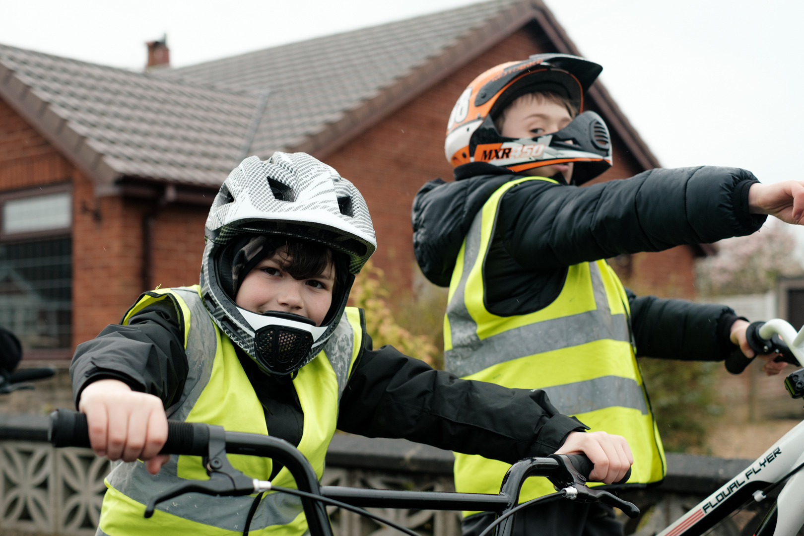 Two young boys on their bikes. They are wearing helmets with chin guards and looking at the camera smiling