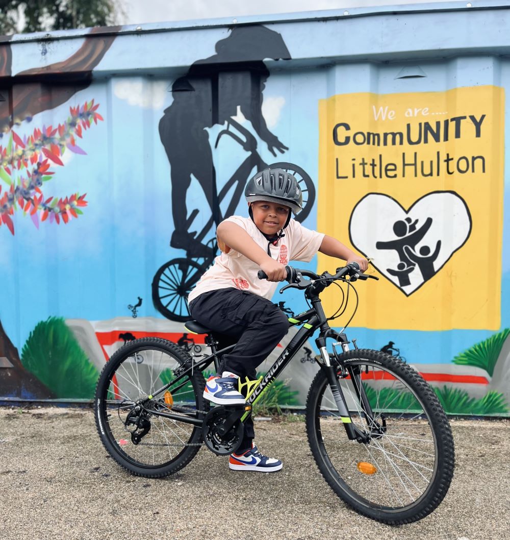 A boy is sat on his cycle in front of a community hub that is decorated with a painting on rider jumping their bike in silhouette