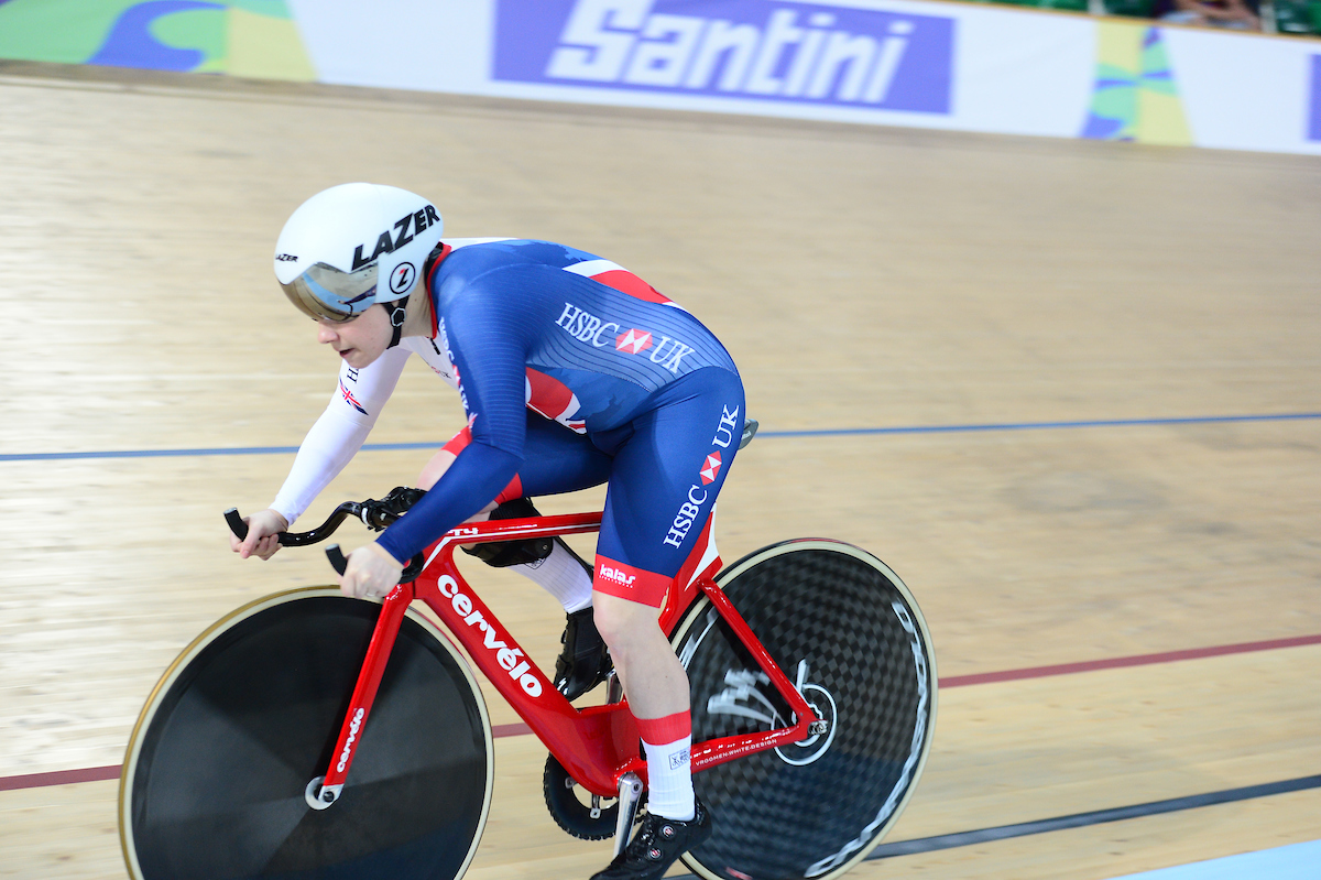 Paralympic cyclist Megan Giglia is riding a bike in a velodrome she is wearing a blue GB uniform and white helmet