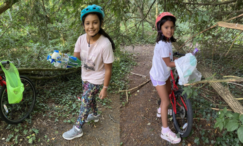 Two girls are picking up litter in a wood with their bicycles in the background