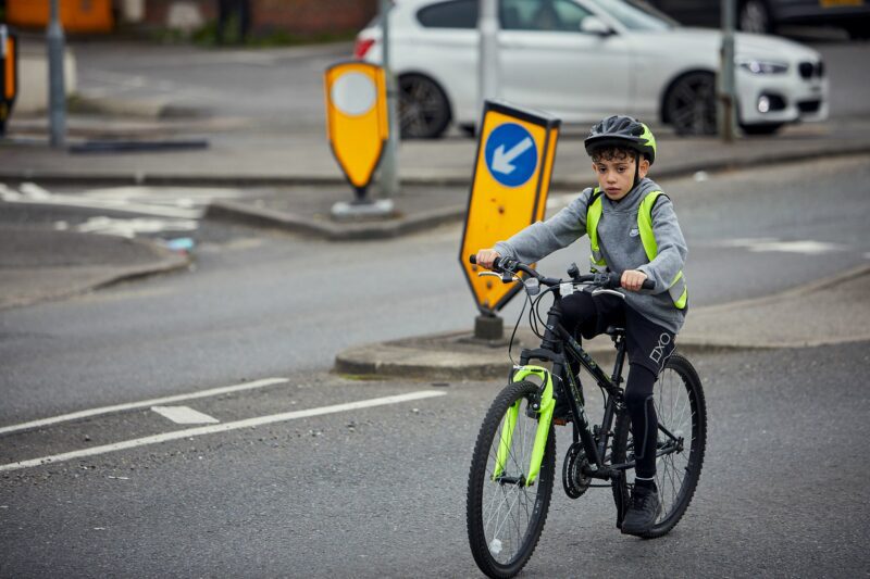 A boy cycling along a road wearing a hi vis vest and a helmet