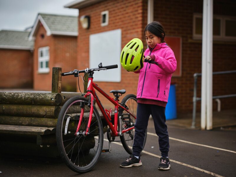 A girl standing next to a bicycle putting a helmet on