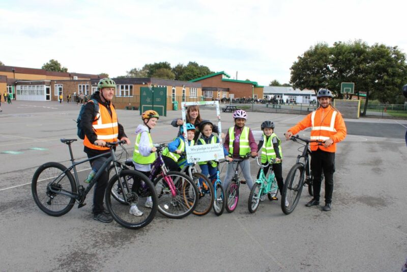 A group of students, teachers and Bikeability instructors posing with their bikes for a photograph in a playground