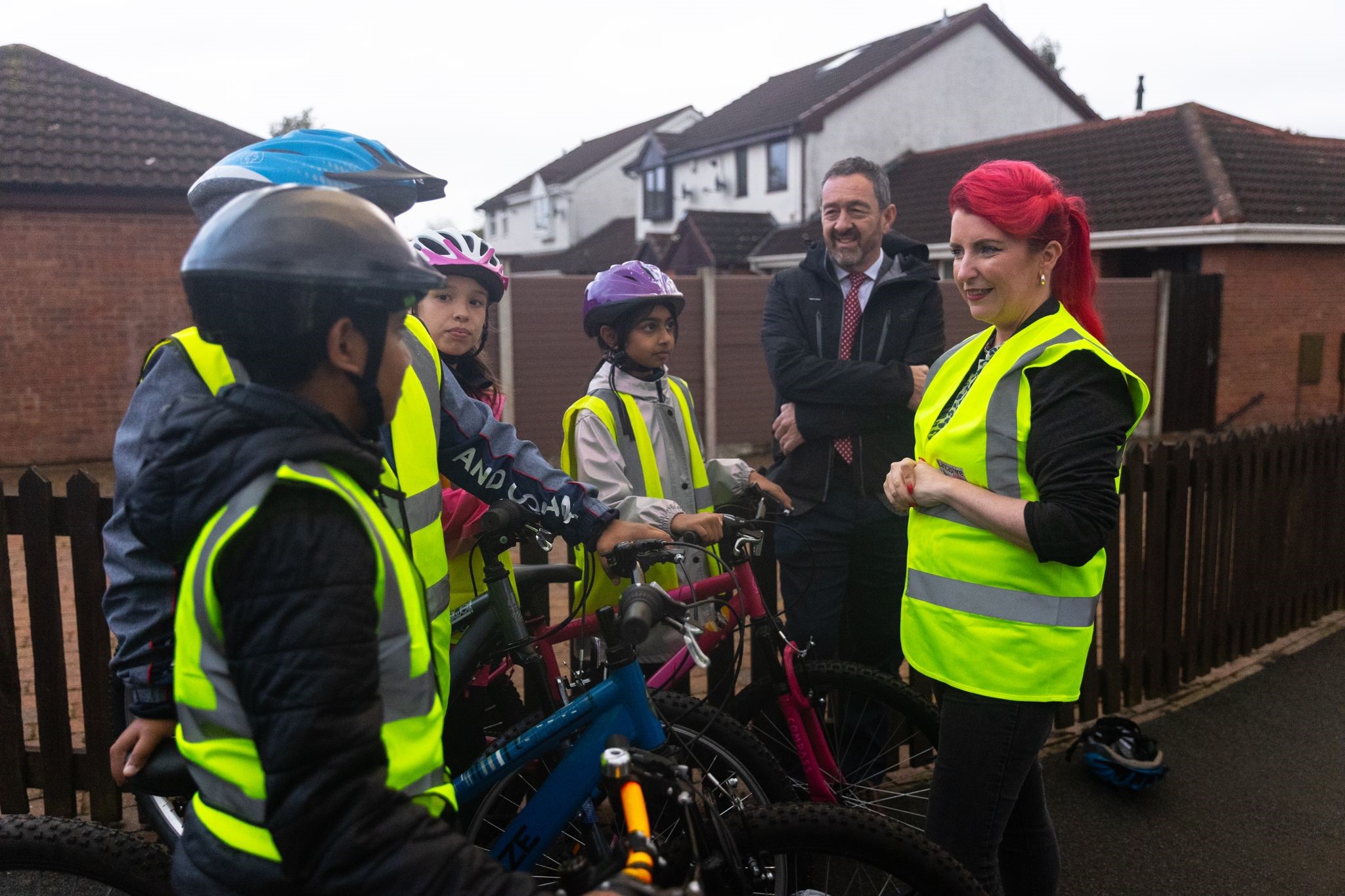 Louise Haigh, secretary of state for transport, is with some Bikeability riders in a playground. They are chatting and wearing hi-vis and helmets