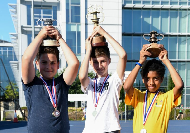 Three children with the gold, silver and bronze trophies hold them up