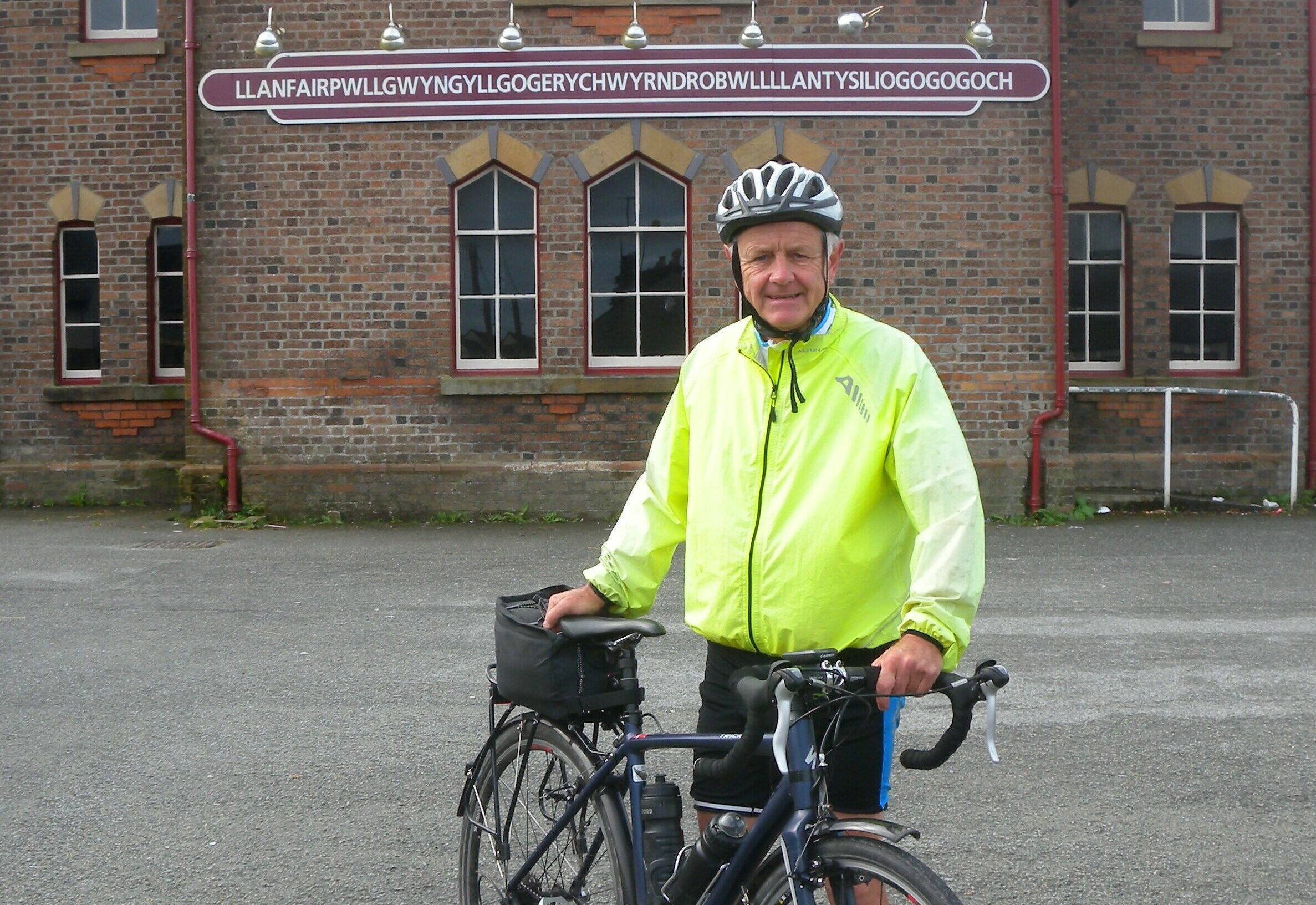 Gareth with his bike in front of a Welsh railway station in Llanfairpwllgwyngyllgogerychwyrndrobwllllantysiliogogogoch